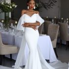 Elegant Anna wedding dress with a fitted crepe skirt, romantic off-the-shoulder sleeves and flowing organza train.
